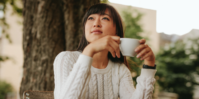 Mulher japonesa sorrindo levemente enquanto segura uma xícara com as suas mãos