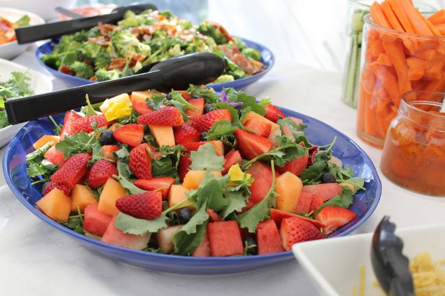 Imagem de salada com frutas na mesa e outras travessas de alimentos em volta
