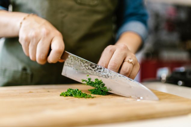 Imagem de uma mulher cortando verduras com uma faca 