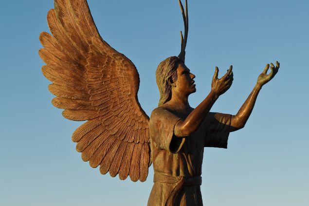 Imagem de uma estátua de um anjo que está com as mãos e a cabeça erguidas ao céu