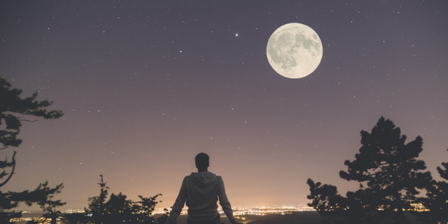 Homem sentado observando a Lua Cheia em um céu estrelado