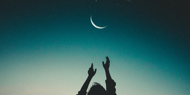 Silhueta de uma mulher com as duas mãos para cima tentando alcançar a Lua no céu estrelado