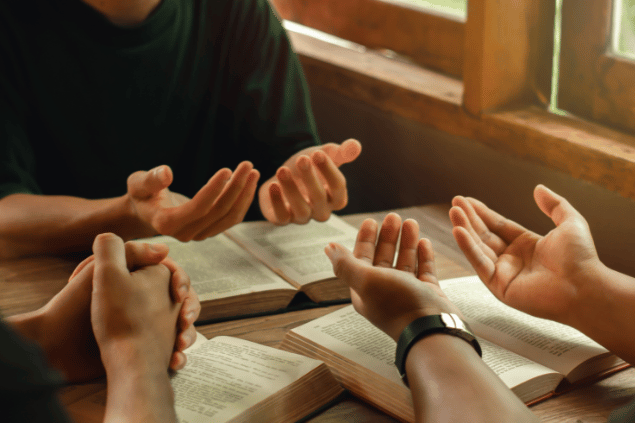 Grupo de cristãos sentados com as mãos para cima em sinal de oração, com as bíblias no centro. 