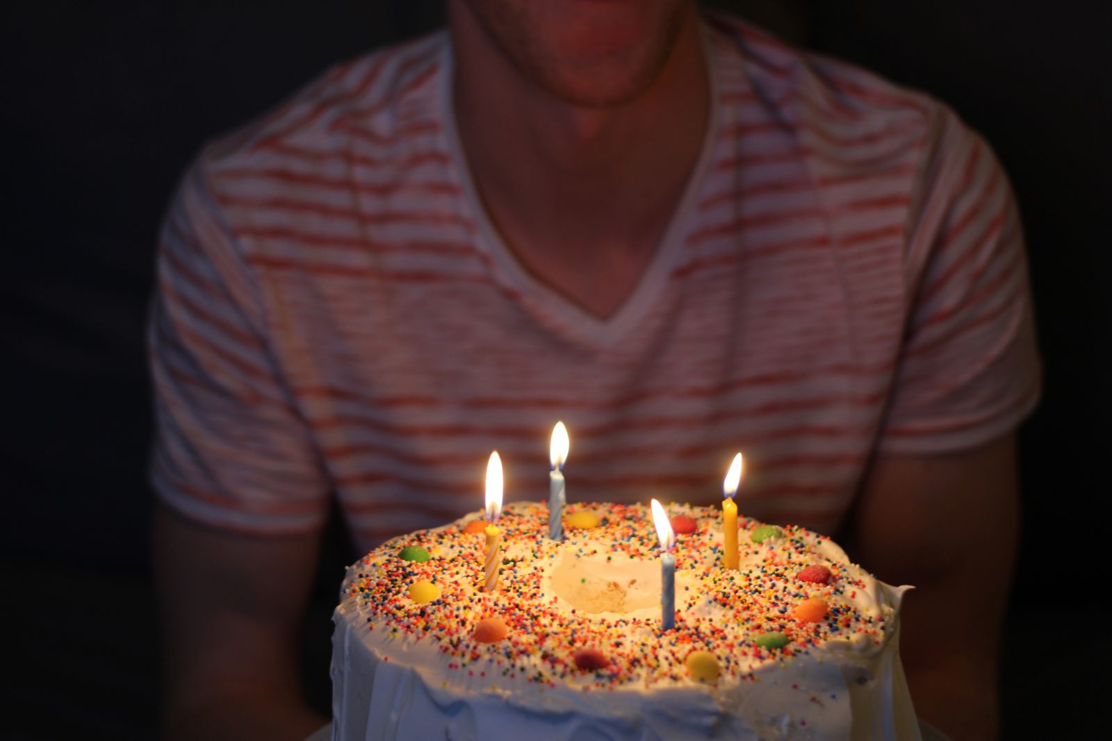 Pessoa segurando seu bolo de aniversário com as velas acesas.