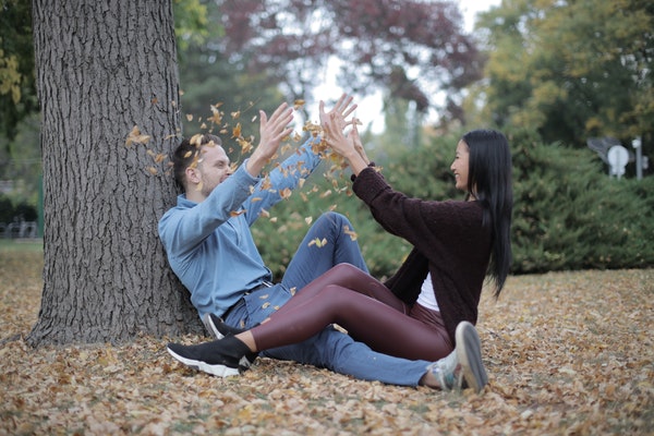 Casal sentado nos pés de uma árvore jogando folhas secas um no outro