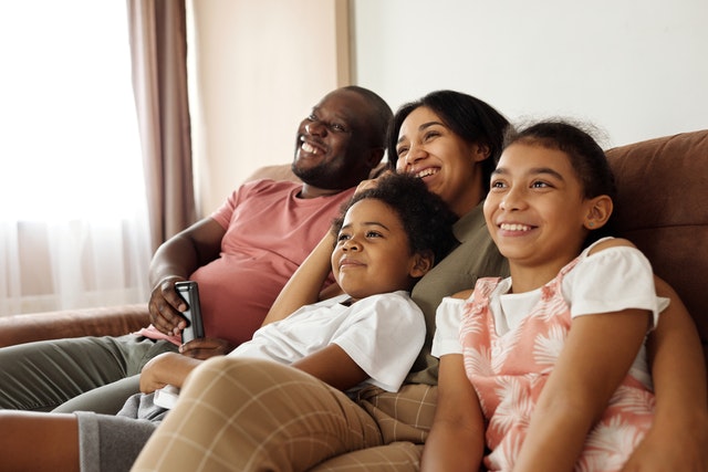 Homem, mulher e crianças negras sentadas num sofá, com expressões sorridentes.