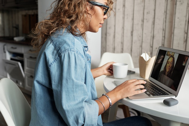Mulher branca sentada em frente à computador, realizando chamada de vídeo.