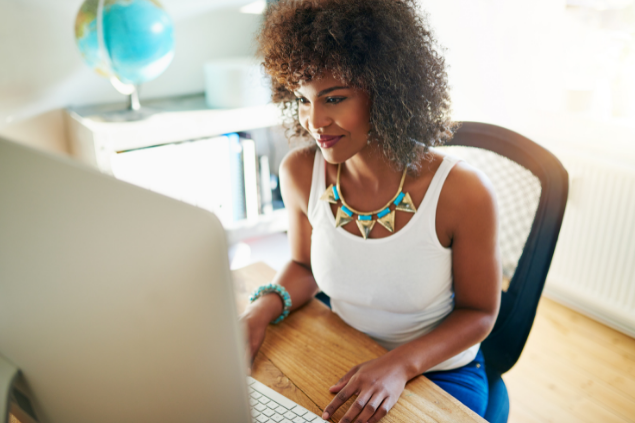 Mulher sentada trabalhando enquanto sorri para a tela do computador