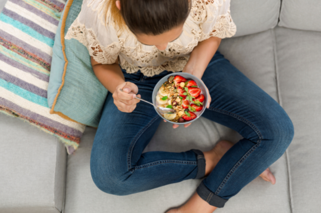 Mulher sentada comendo um pote com frutas