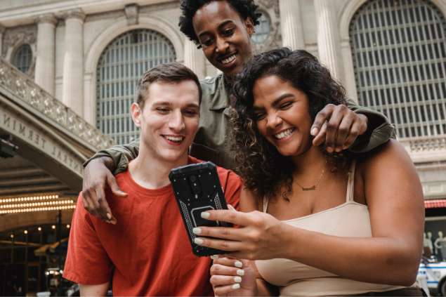 Três amigos rindo enquanto olham algo no celular