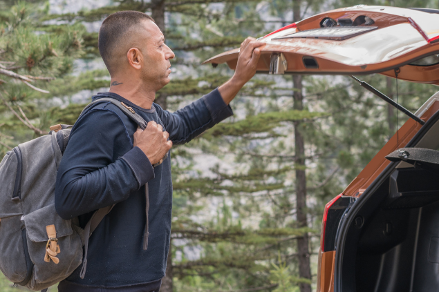 Homem com mochila nas costas fechando o porta malas de um carro