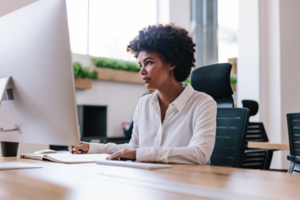 Mulher mexendo no computador que está em cima de uma mesa de madeira