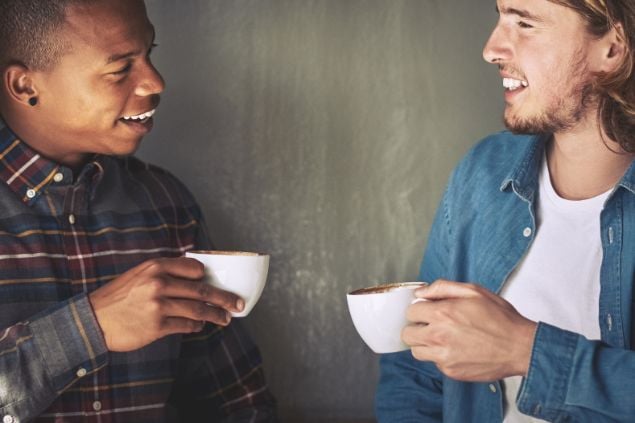 Dois rapazes, cada um com uma xíacara na mão, conversando e sorrindo