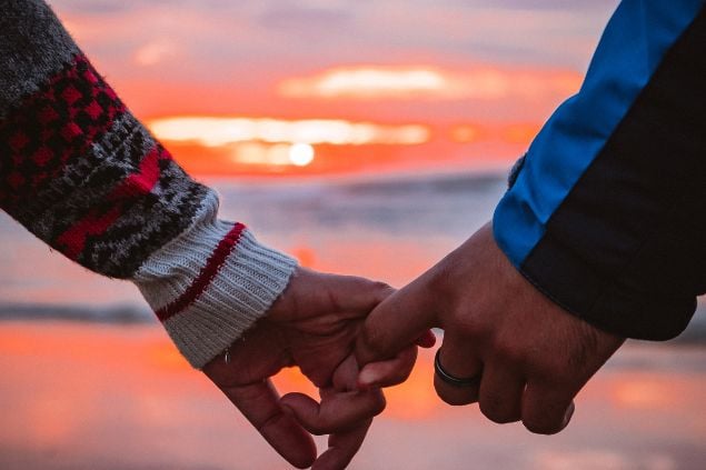 Mãos dadas de frente para uma praia ao pôr-do-sol