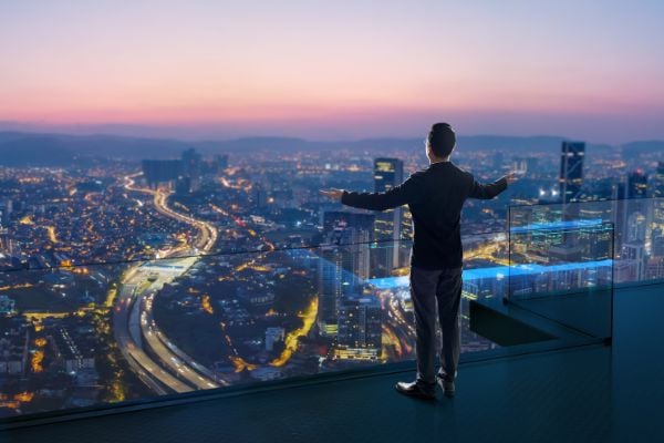 Homem de braços abertos em um terraço, observando a paisagem urbana