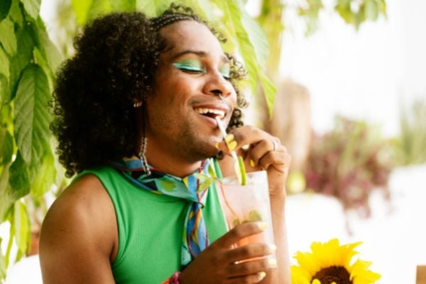 Homem de sombra e blusa verde tomando um suco e sorrindo