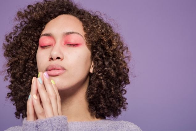 Imagem de uma mulher com os olhos fechados e com as mãos juntas perto dos lábios como se estivesse fazendo uma oração