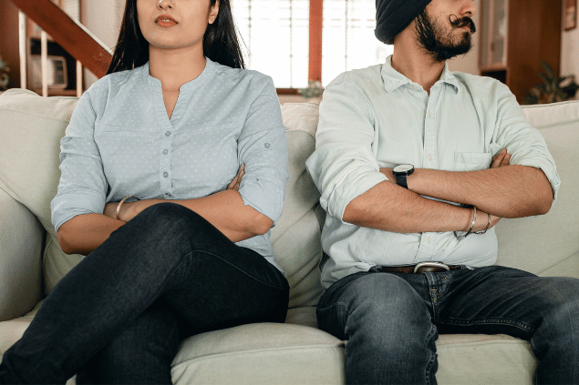 Casal sentado no sofá com braços cruzados. Eles passam por problemas em seu relacionamento. 