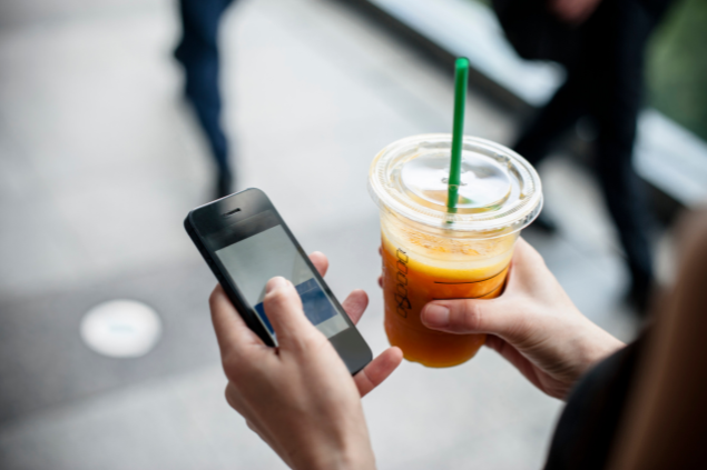 Mãos segurando um celular e um suco de laranja