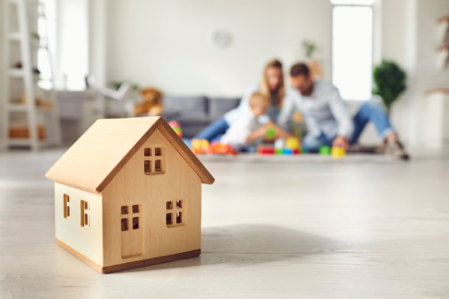 Casal brincando com o filho e a frente, uma miniatura de casa feita de madeira