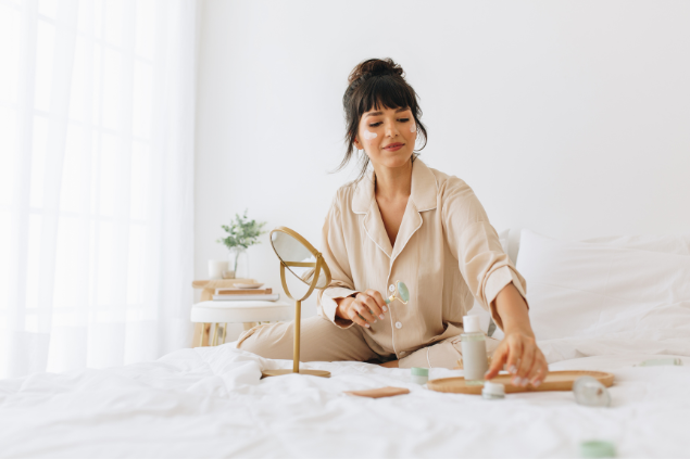 Mulher sentada em sua cama fazendo skincare