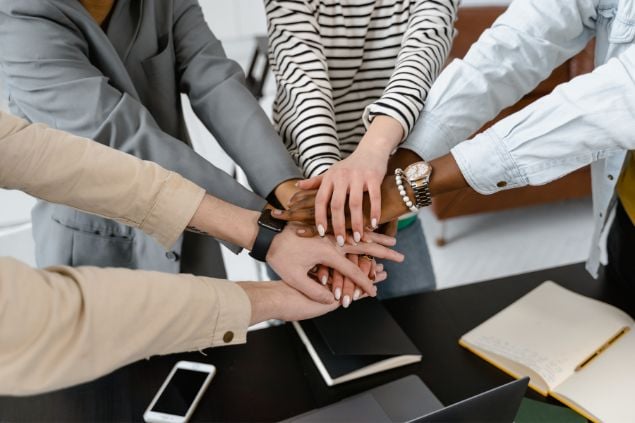 Imagem de várias pessoas em um ambiente de trabalho reunidas e com as mãos uma sobre a outra.