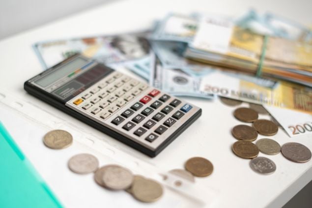 Imagem de uma mesa e sobre ela uma calculadora, moedas e dinheiro em espécie, representando o conceito de gestão financeira.