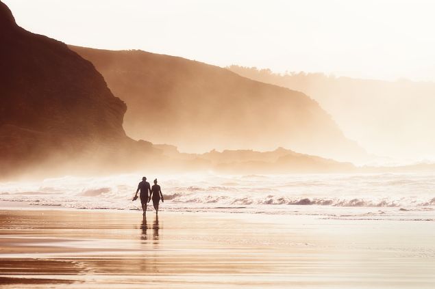 Imagem de um casal caminhando na praia em um lindo fim de tarde.