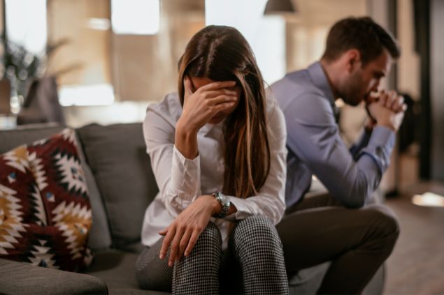 Imagem de um jovem casal triste e infeliz, sentado em uma sofá em uma sala de estar.