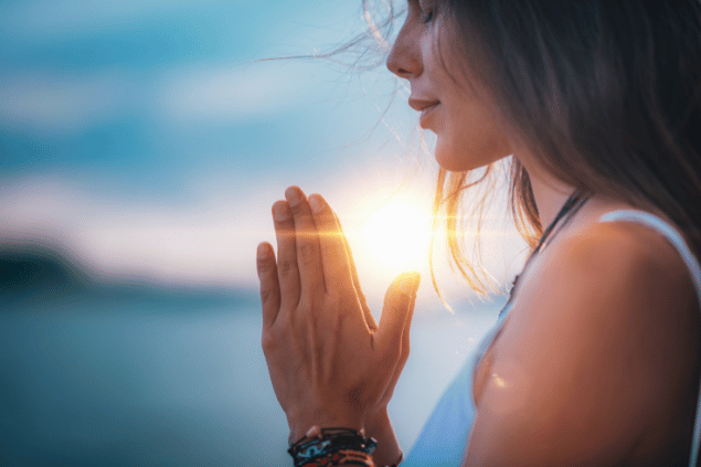 Imagem de um lindo pôr do Sol e em destaque a foto de uma mulher de lado, com as mãos juntas em posição de oração, simbolizando que está rezando para o São Valetim, para proteger o seu relacionamento.