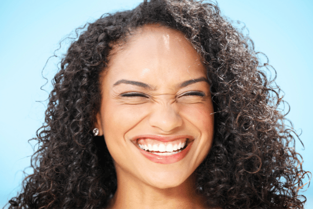 Imagem de uma mulher de cabelos cacheados esbanjando um lindo e largo sorriso, trazendo o conceito de sorrir sempre.