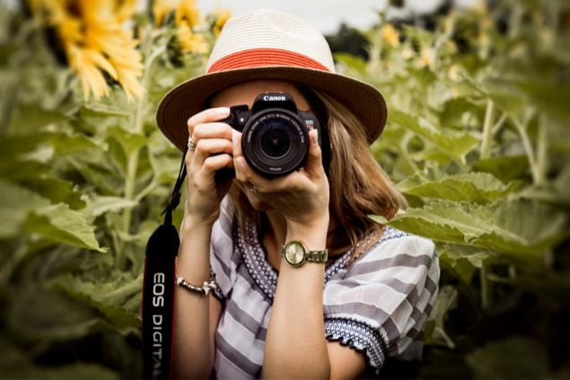 Imagem de uma mulher fotógrafa em meio a uma floresta segurando uma câmera e registrando lindas espécies da fauna e da flora.