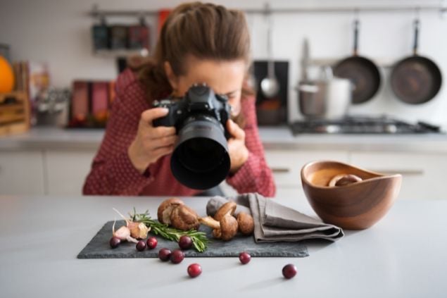 Imagem de uma mulher fotógrafa em uma cozinha fazendo fotos de ingredientes para um prato culinário.