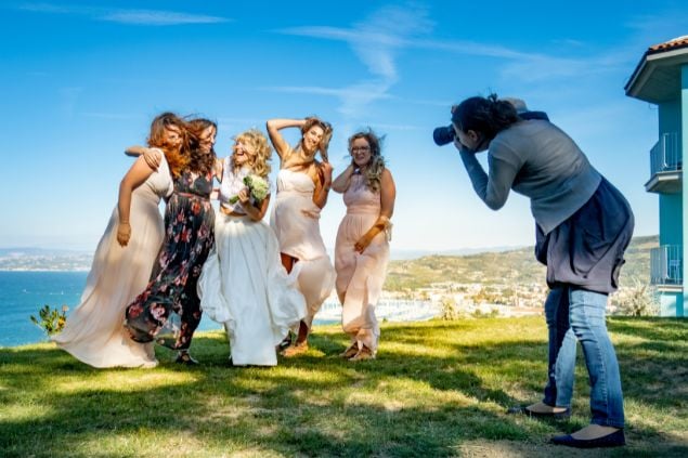 Imagem de uma mulher fotógrafa fazendo fotos de uma noiva e suas madrinhas.