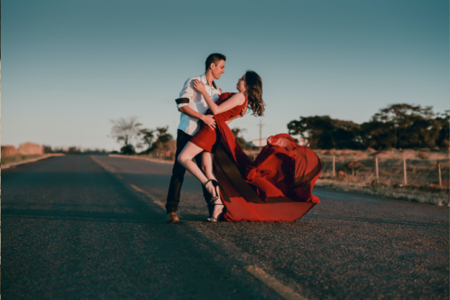 Homem e mulher de vestido dançando no meio de uma avenida