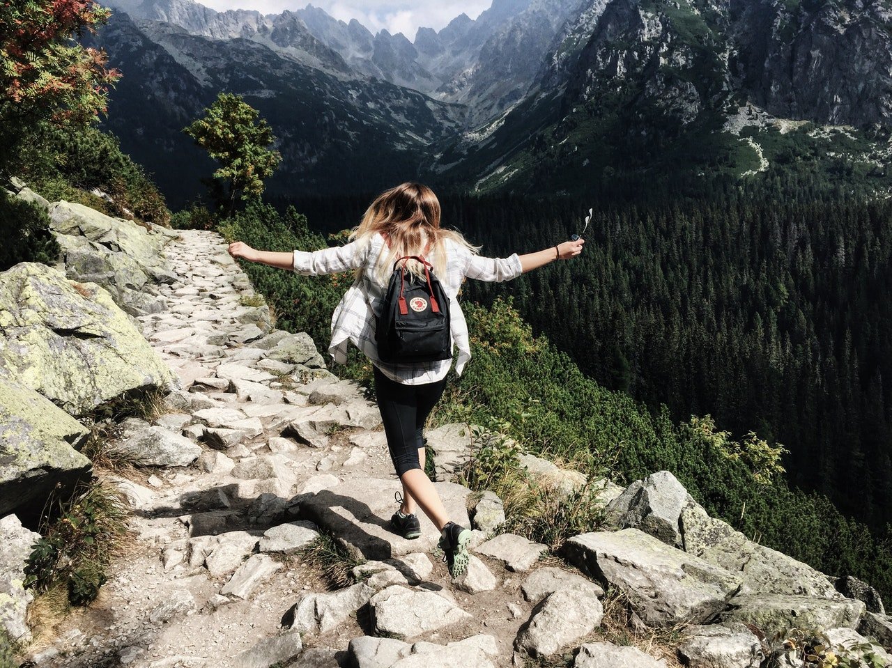 Mulher andando em montanha, a beira de um penhasco, com os braços abertos, e sozinha.