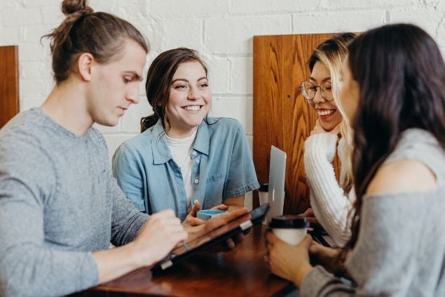 Grupo de 3 mulheres e 1 homem conversando alegremente em uma mesa.