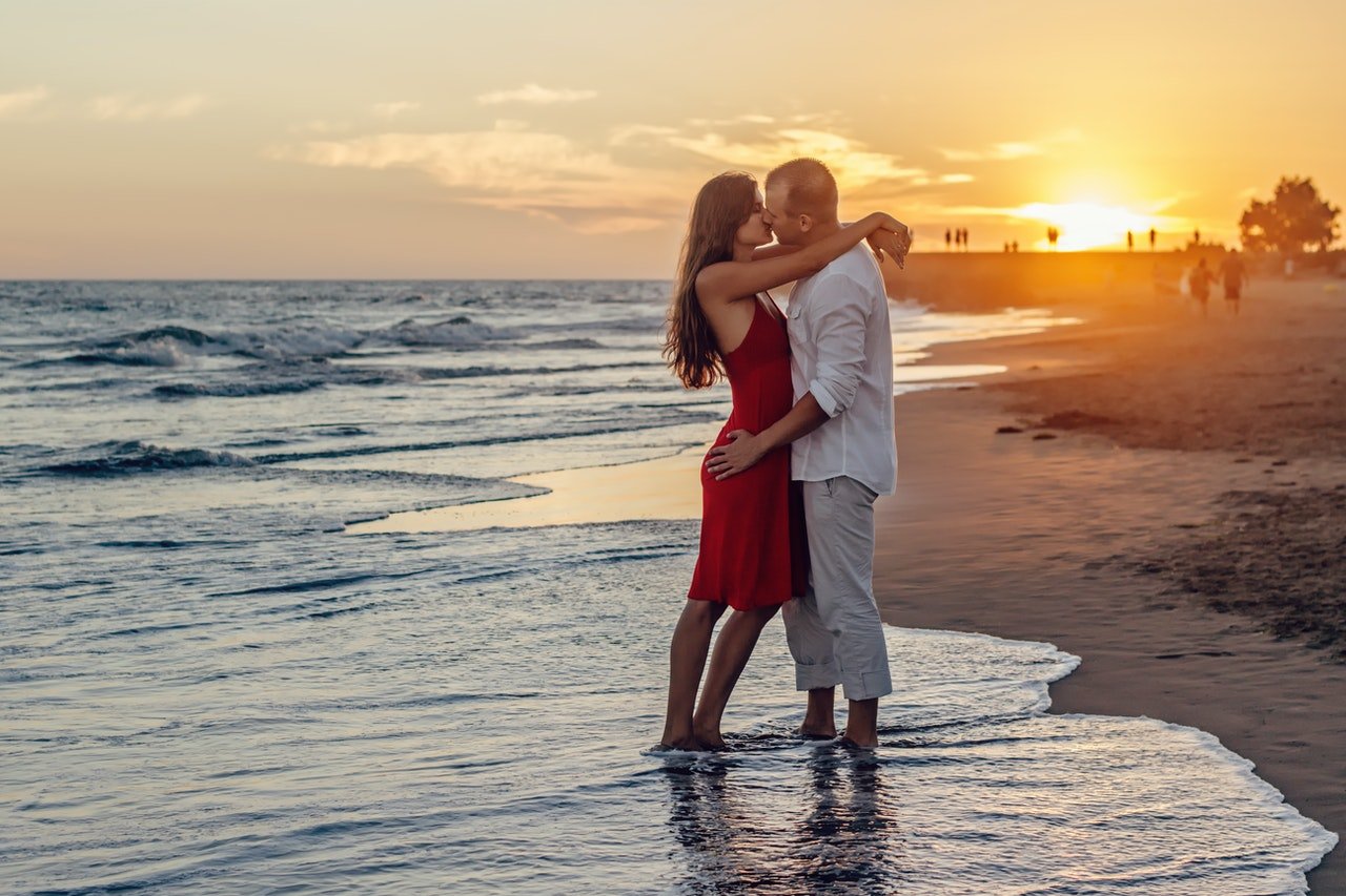 Homem e mulher, em praia, se beijando durante o pôr-do-sol.