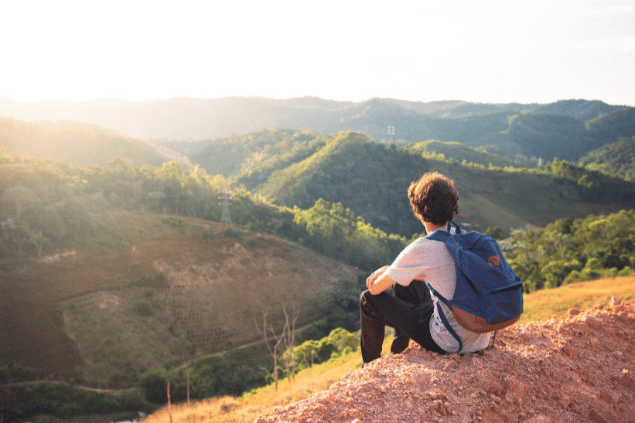 Homem sentado em cima de uma pedra enquanto observa várias montanhas