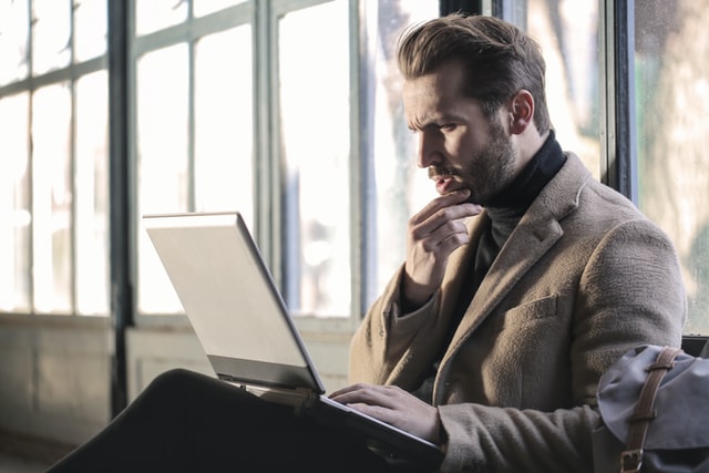 Homem branco com notebook no colo e expressão confusa.