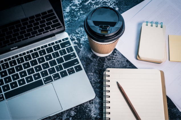 Mesa organizada com coisas de trabalho, como computador, café e blocos de nota