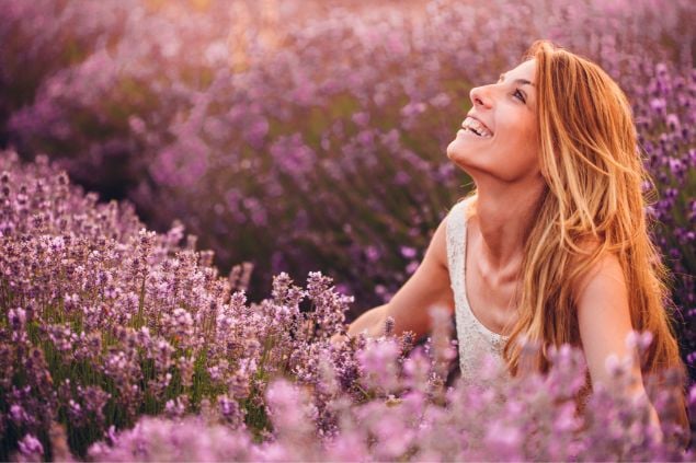 Mulher feliz e sorrindo para o céu no meio de uma plantação de lavanda