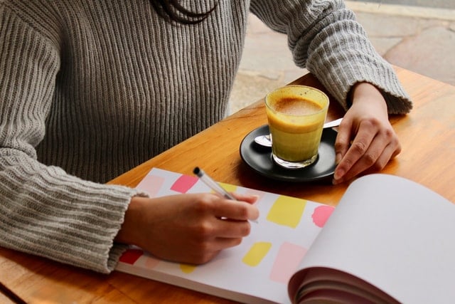 Mulher branca escrevendo em caderno.