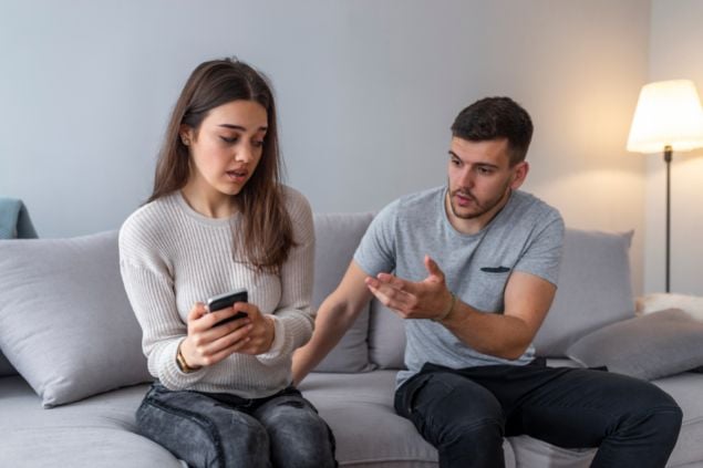 Mulher ciuemnta olhando o celular do marido, enquanto ele reclama