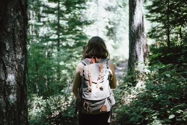 Mulher branca de costas com mochila na floresta.