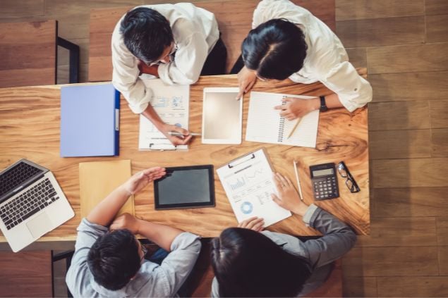 Várias pessoas reunidas em torno de uma mesa de trabalho com vários notebooks e papeis