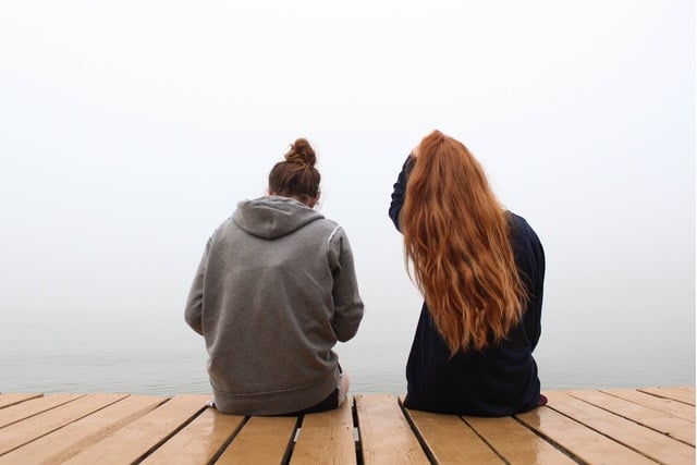 Jovens brancas sentadas de costas num píer.