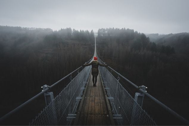 Mulher caminhando em uma longa e alta ponte de madeira.