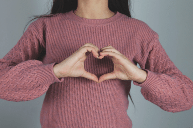 Mulher usando um suéter na cor rosa queimado fazendo coração com as mãos