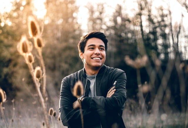 Homem sorrindo de braços cruzados num campo.